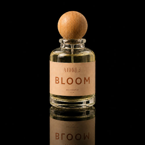A clear glass perfume bottle with a round wooden stopper and a beige label reading 'ATHRISE BLOOM', centered on a black reflective background.