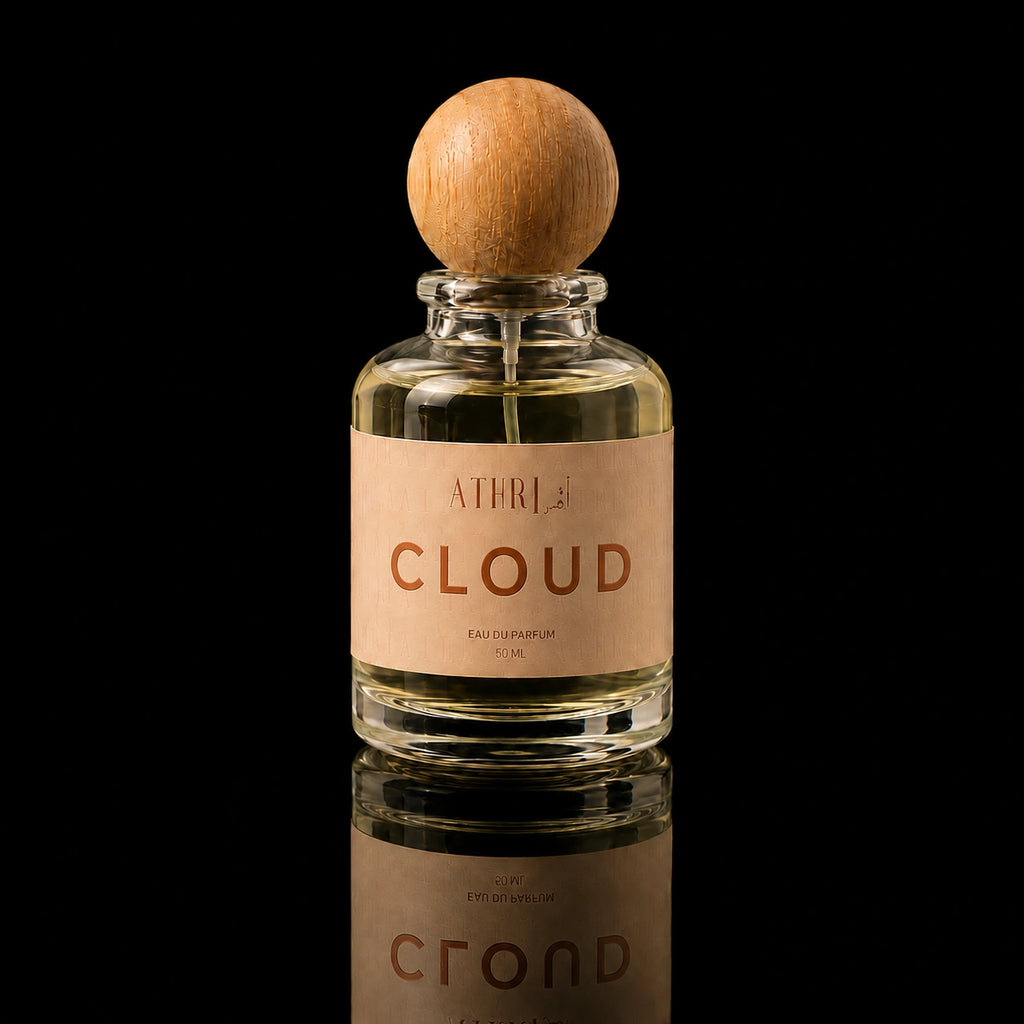 A clear glass perfume bottle with a round wooden stopper and a beige label reading 'ATHRISE BLOOM', centered on a black reflective background.