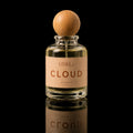 A clear glass perfume bottle with a round wooden stopper and a beige label reading 'ATHRISE BLOOM', centered on a black reflective background.