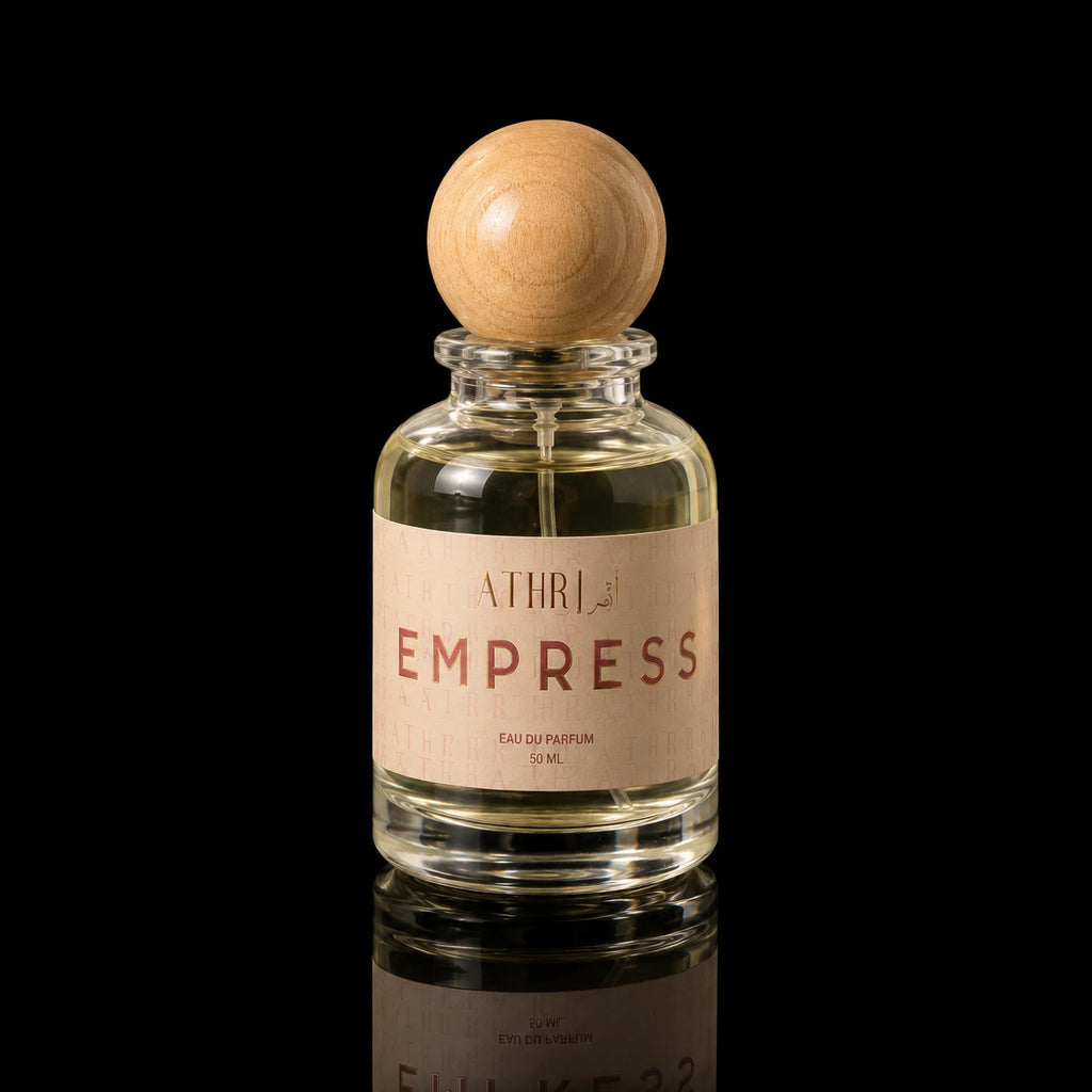 A clear glass perfume bottle with a light wood spherical cap and a beige label reading 'ATHRI EMPRESS EAU DE PARFUM 50 ML', photographed on a black reflective surface.