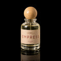 A clear glass perfume bottle with a light wood spherical cap and a beige label reading 'ATHRI EMPRESS EAU DE PARFUM 50 ML', photographed on a black reflective surface.