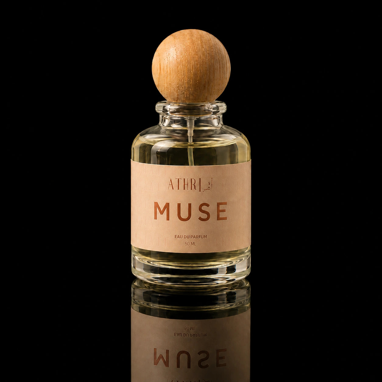 A clear glass perfume bottle with a round light wood cap and a beige label reading 'ATHLE MUSE', photographed against a black background with a reflection below.