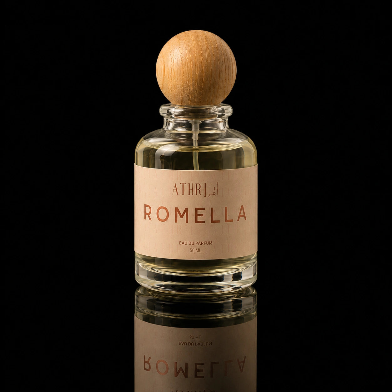 A clear glass perfume bottle with a round light wood cap and a beige label reading ATHRI ROMELLA, photographed against a black background with a reflection below.