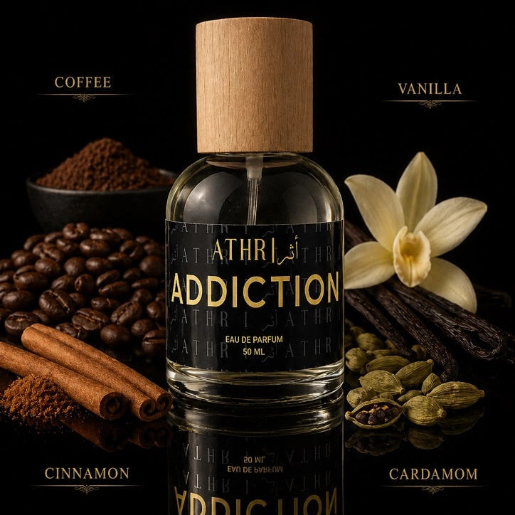 Athr Addiction perfume bottle with coffee beans, vanilla flower, cinnamon sticks, and cardamom on a dark background.