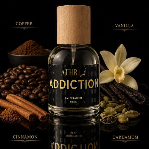 Athr Addiction perfume bottle with coffee beans, vanilla flower, cinnamon sticks, and cardamom on a dark background.