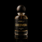 A 50 ml bottle of Athri Cocoverera Eau de Parfum, featuring a clear glass bottle filled with amber-colored fragrance liquid, a black label with gold lettering, and a dark wooden spherical cap, set against a solid black background with a subtle reflection below.