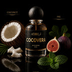 A bottle of ATHRiCOCOVERA coconut and fig eau de parfum, 50 ml, displayed on a reflective black surface with fresh coconut, figs, mint leaves, and mint buds around it.