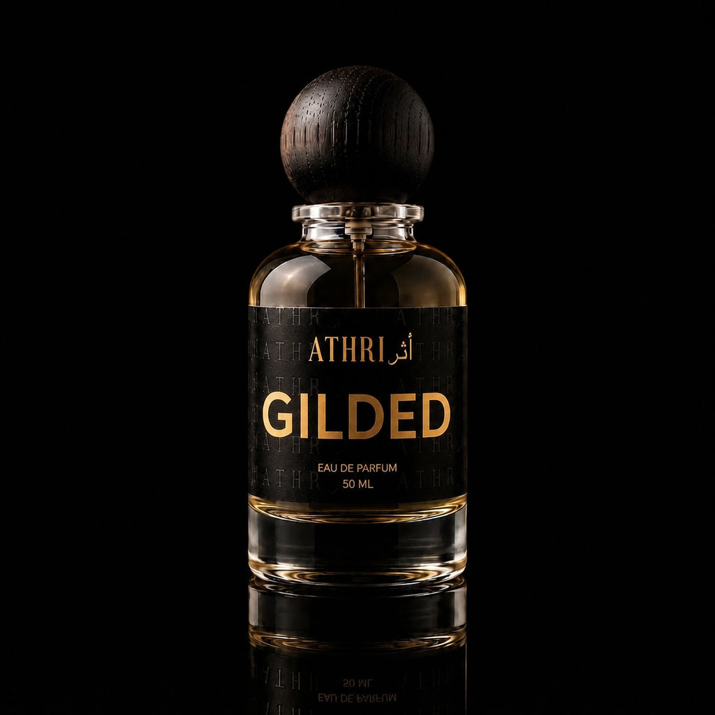 A 50 ml bottle of Athri Gilded Eau de Parfum with a black label and a dark wooden spherical cap, set against a solid black background with a subtle reflection below.