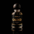 A 50 ml bottle of Athri Gilded Eau de Parfum with a black label and a dark wooden spherical cap, set against a solid black background with a subtle reflection below.