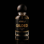A 50 ml bottle of Athri Gilded Eau de Parfum with a black label and a dark wooden spherical cap, set against a solid black background with a subtle reflection below.