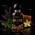 A bottle of Gilded Eau de Parfum by Athri, styled with lavender, mint, a yellow flower, and honey on a reflective black surface. Text labels identify the scent notes: Lavender, Honey, Mint, and Benzoin.