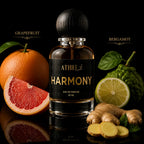 A bottle of ATHRI AHR Harmony Eau de Parfum centered on a black reflective surface, surrounded by citrus and spice ingredients including grapefruit, bergamot, lime, ginger, and green leaves. The bottle has a black label with gold lettering and a dark wooden cap.