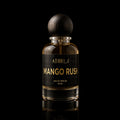 A 50 ml bottle of Athri Mango Rush Eau de Parfum, featuring a clear glass bottle filled with amber-colored fragrance liquid, a black label with gold lettering, and a dark wooden spherical cap, set against a solid black background with a subtle reflection below.