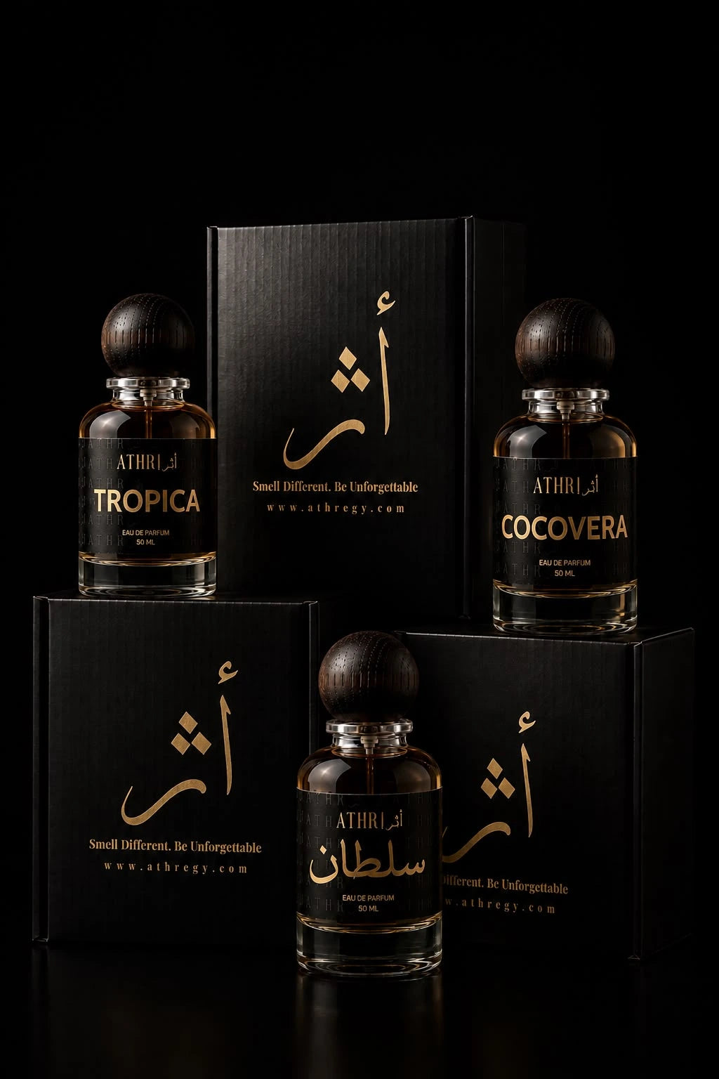Four perfume bottles and matching black boxes arranged on a black studio background. The bottles are clear glass with amber-brown liquid and dark round caps, labeled with gold text including ATHRI, TROPICA, and COCOVERA.