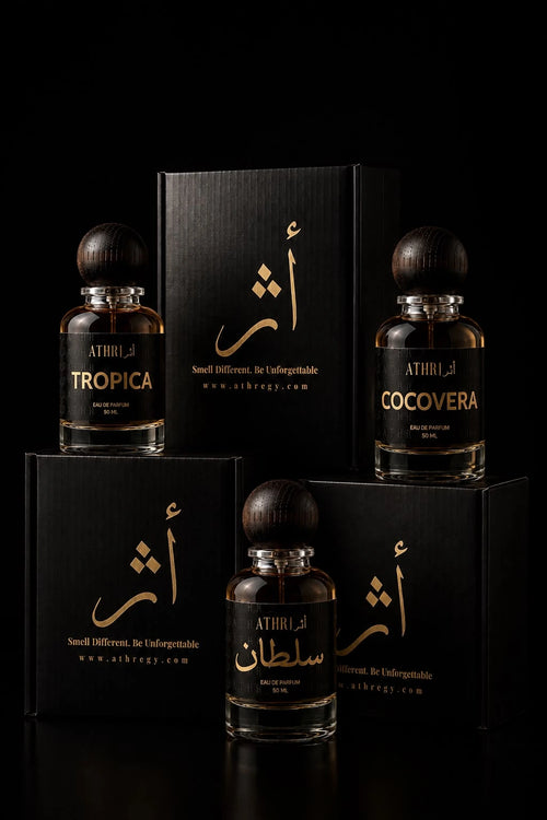 Four perfume bottles and matching black boxes arranged on a black studio background. The bottles are clear glass with amber-brown liquid and dark round caps, labeled with gold text including ATHRI, TROPICA, and COCOVERA.
