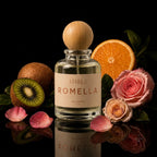 A bottle of Aithria Romella Eau de Parfum with a wooden cap, set against a black background with pink roses, kiwi, and orange slices around it.